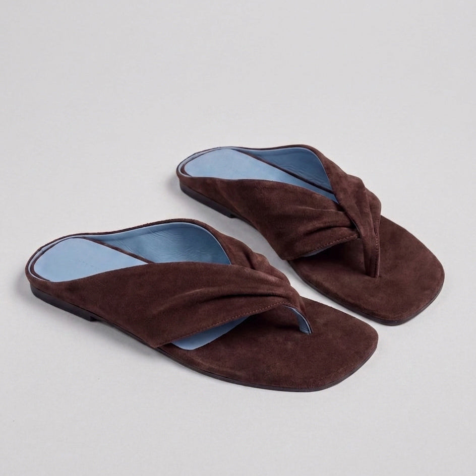 Pair of brown slippers with blue soles on a light gray background