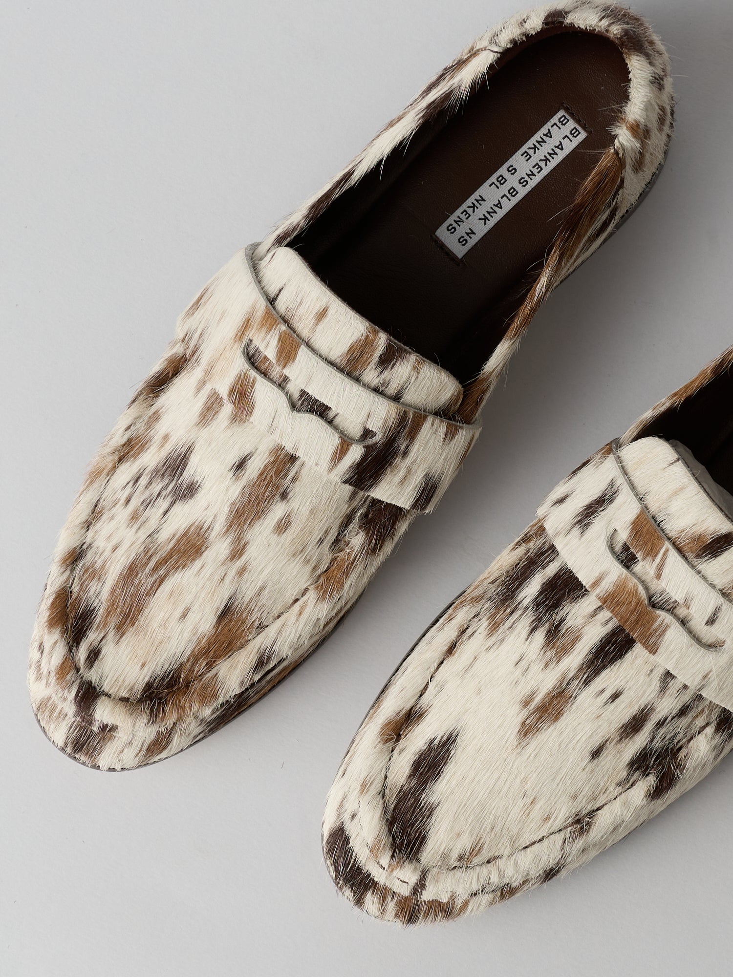 Pair of cow print loafers on a light gray background