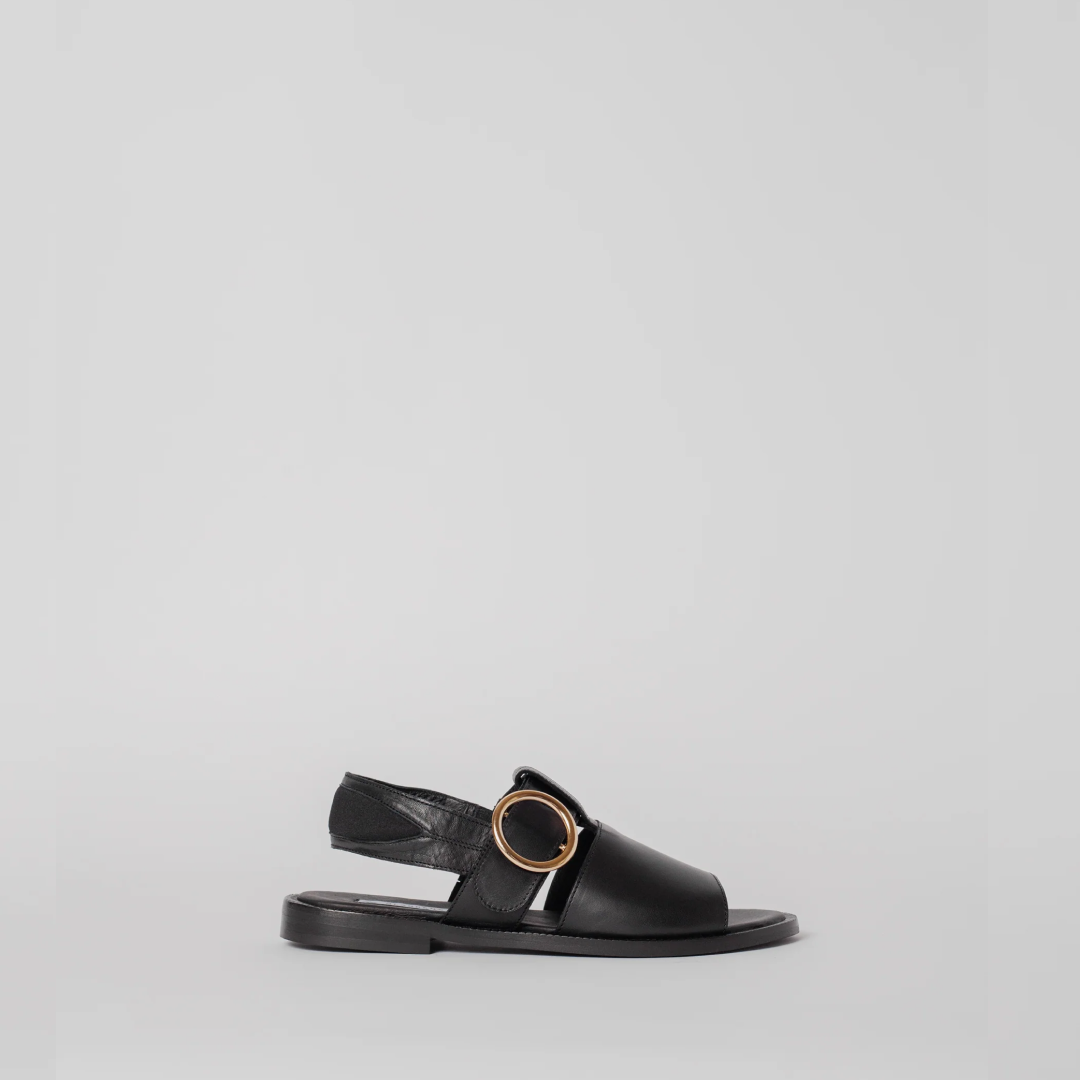 Black sandal with a gold ring on a light gray background